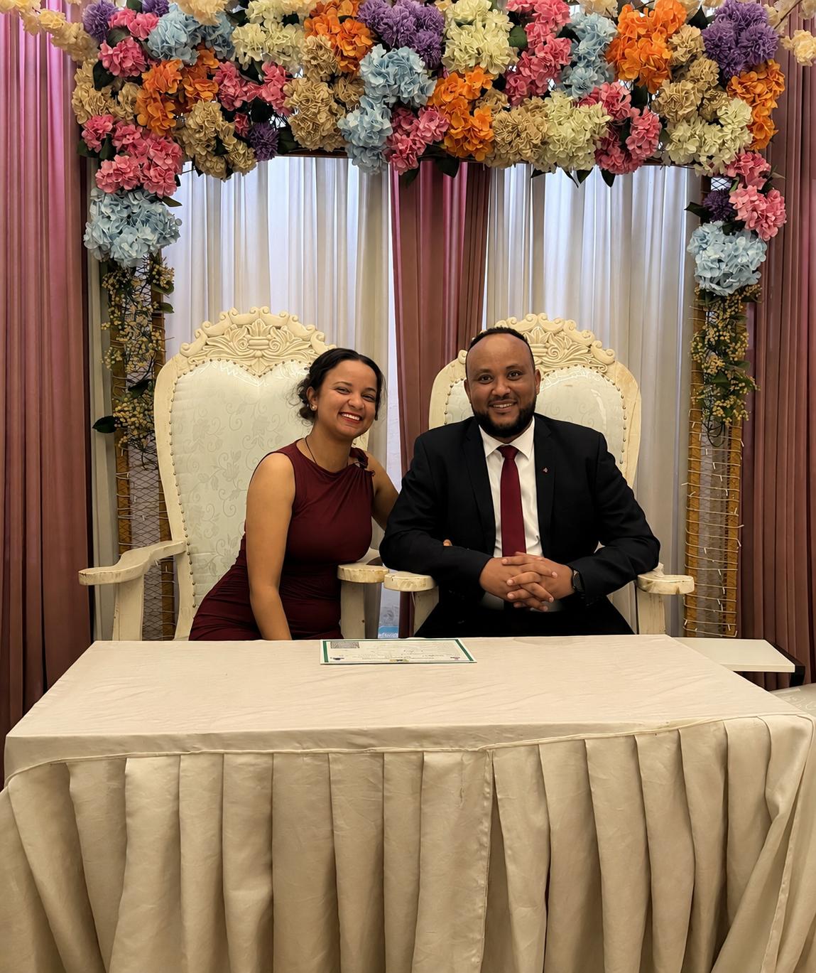 Miss Hiwot & Dr. Bisrat seated beneath a floral arch